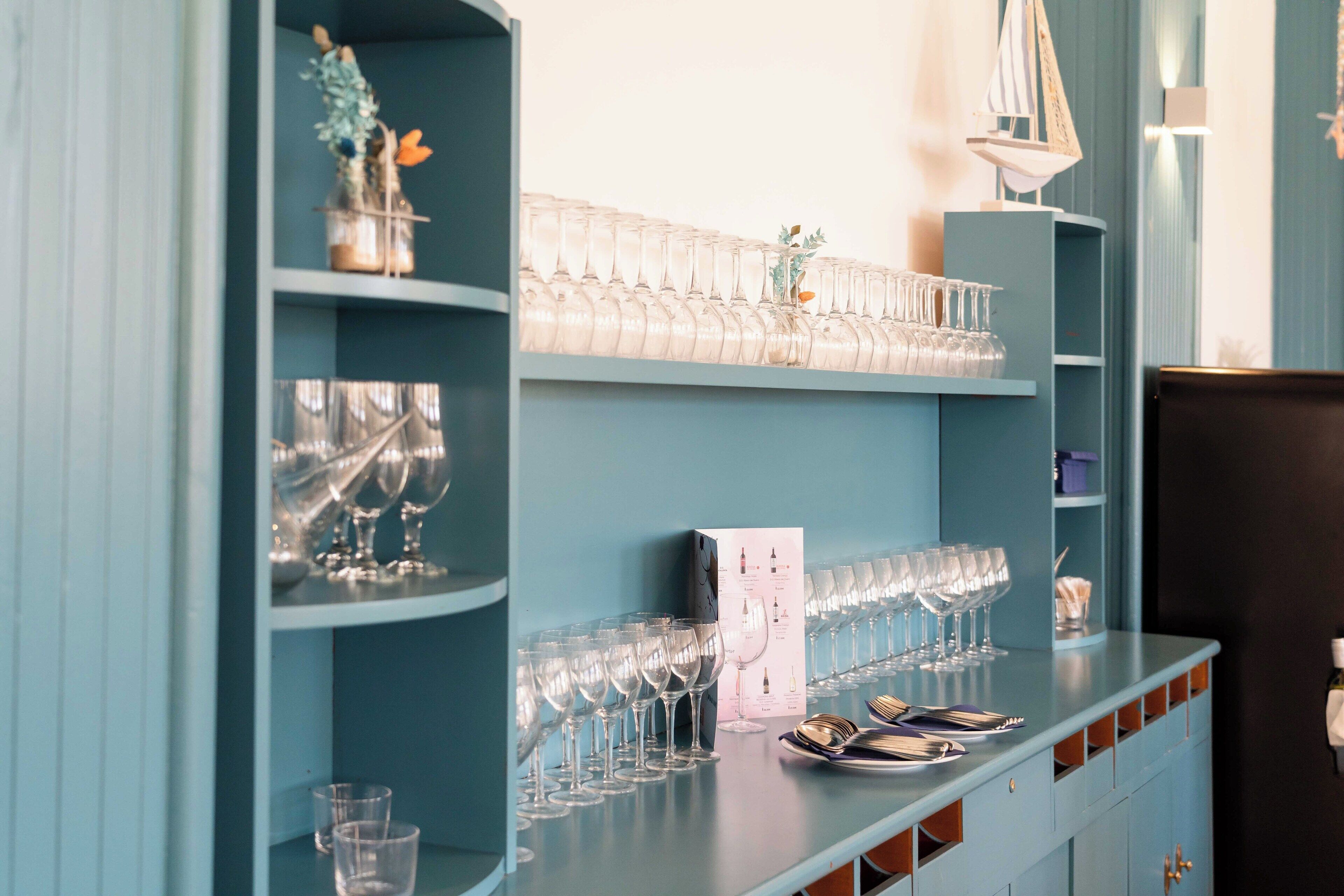 A bar area with shelves of wine glasses and a counter with plates and cutlery.