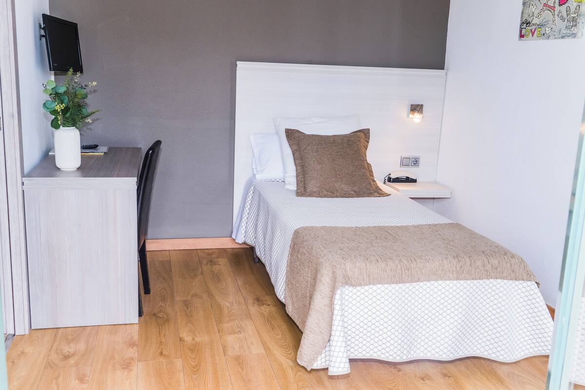 Un dormitorio con cama, mesita de noche y escritorio con silla.