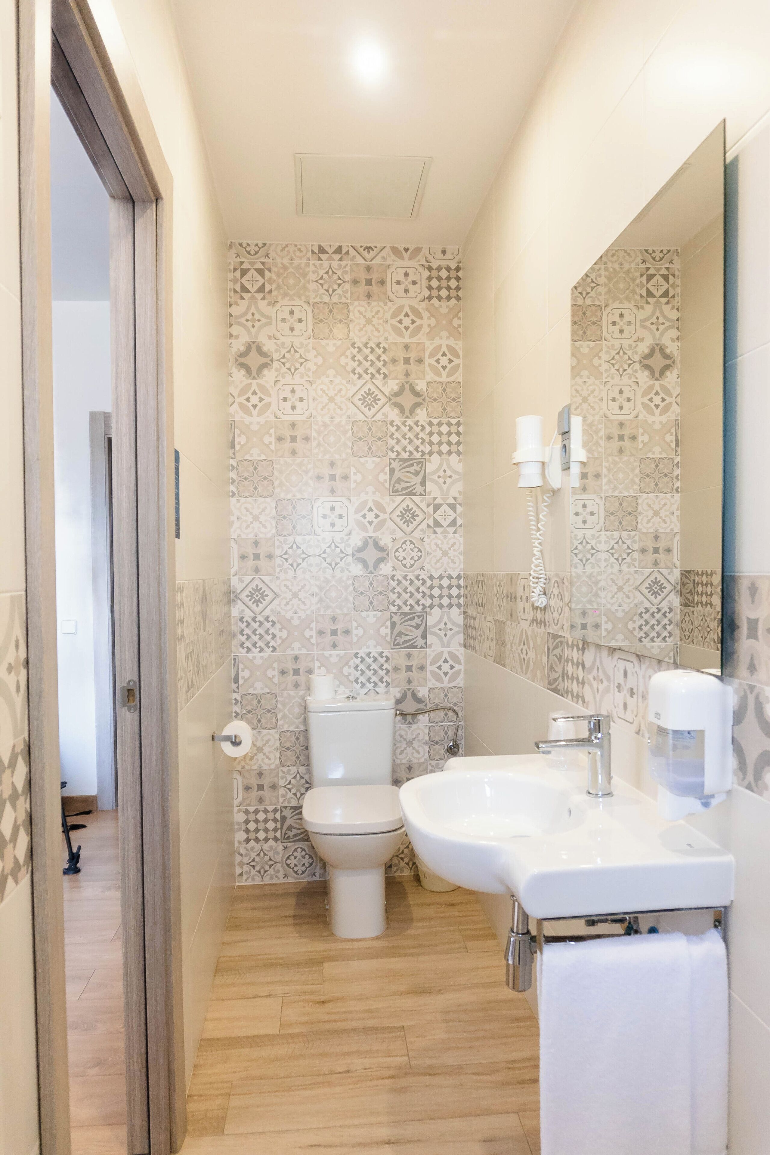 A bathroom with patterned tiles, a toilet, a sink with a mirror, and a towel rack.