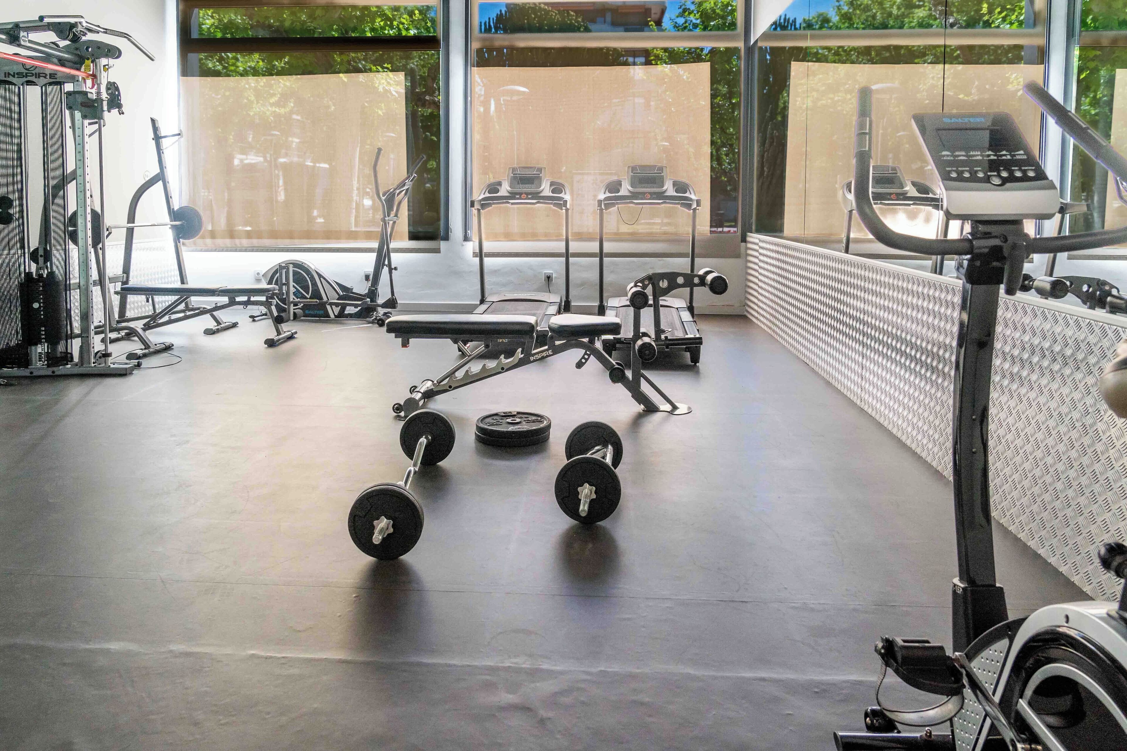 Un gimnasio con diversos equipos de ejercicio, incluyendo una cinta de correr, elíptica y pesas libres.