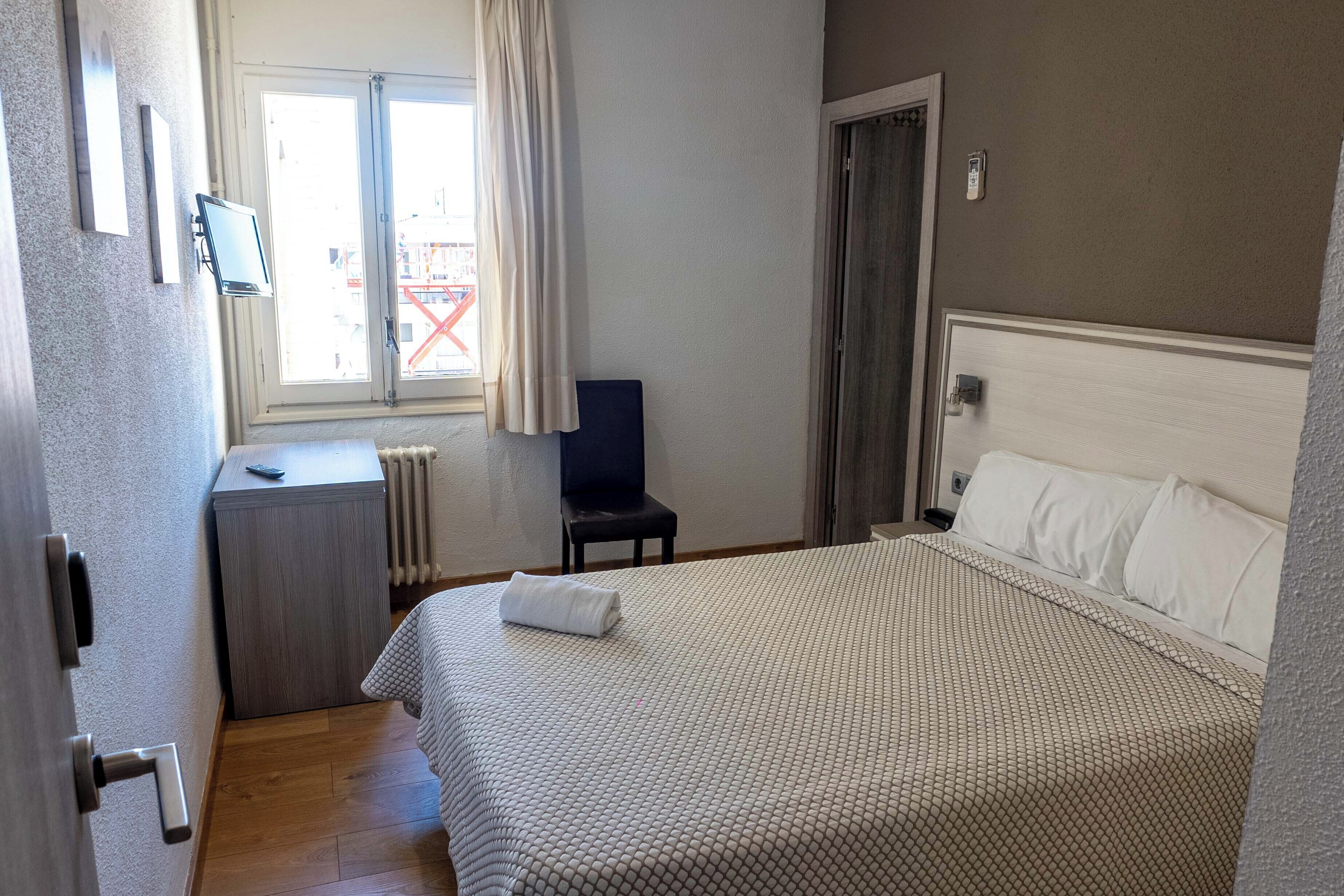 Habitación de hotel con cama, escritorio, silla, radiador y ventana con cortinas.