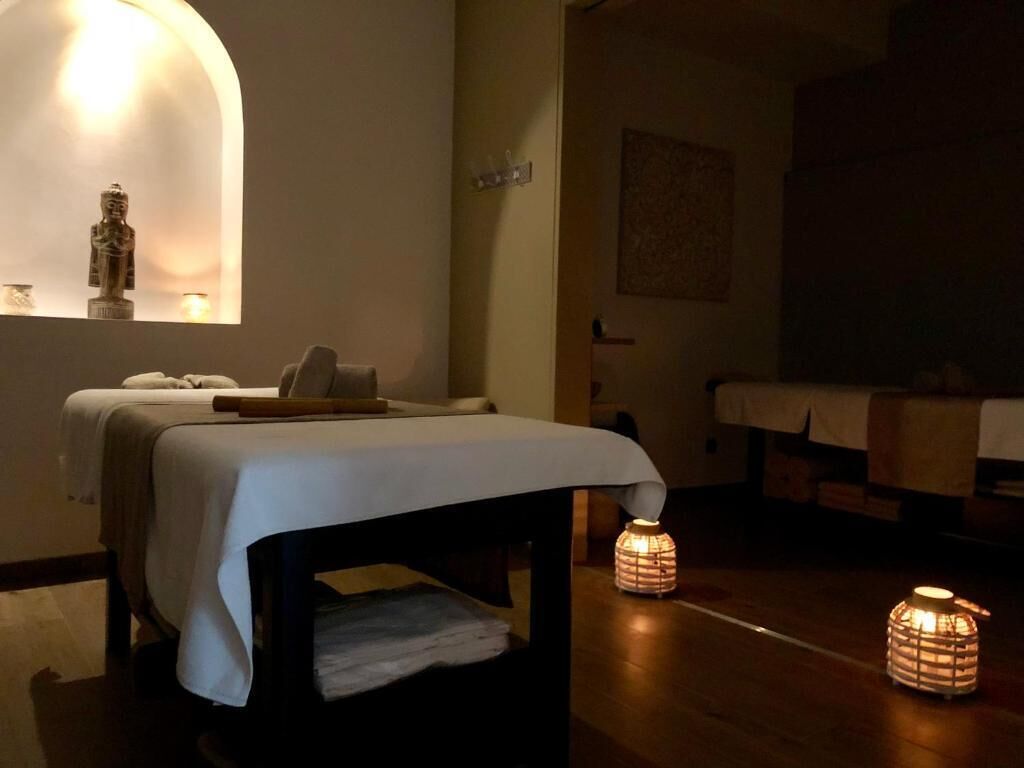 Una habitació amb un llit, una taula petita i dues làmpades fixades a la paret.