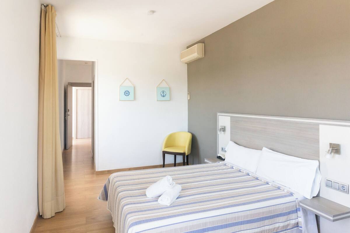 Una habitación de hotel con una cama, una silla, una mesita de noche y un aire acondicionado de pared.