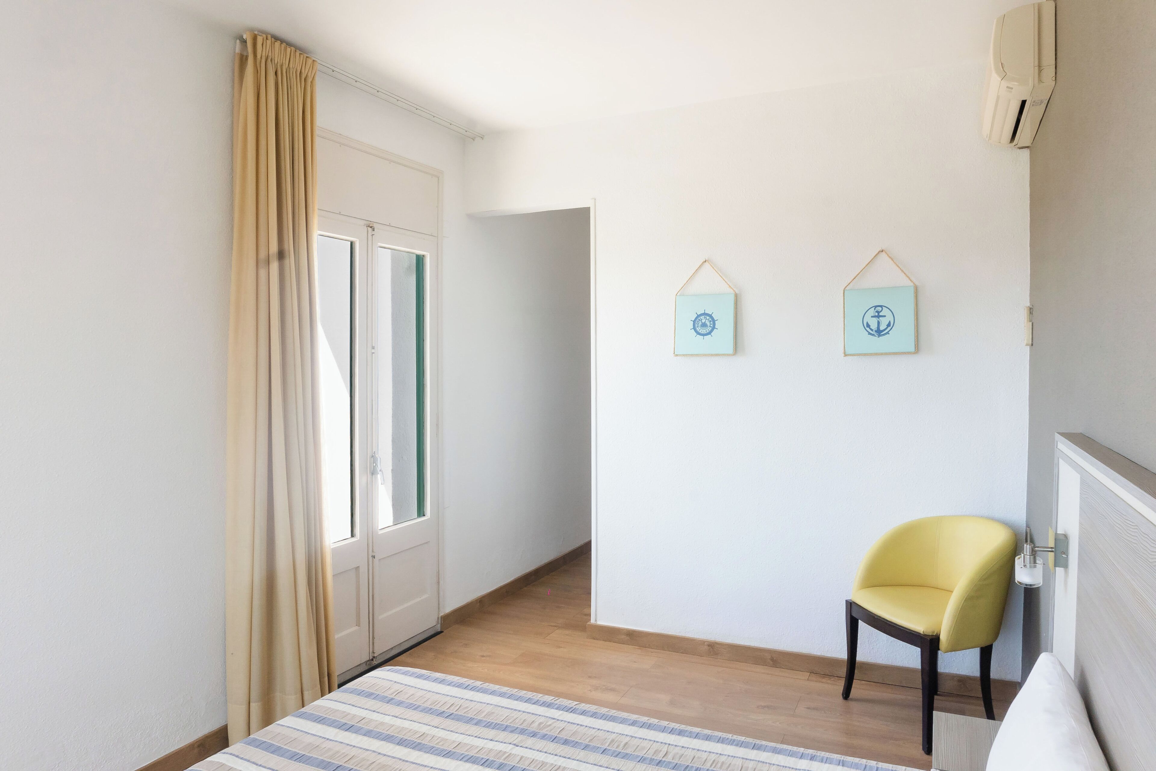 Una habitación con una cama, una silla, una puerta y dos cuadros colgados en la pared.