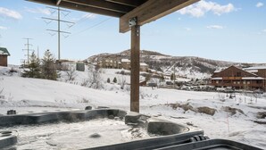 Ein Whirlpoolbereich mit einer Holzkonstruktion darüber, eine verschneite Landschaft mit Gebäuden im Hintergrund und Stromleitungen.