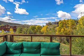 A wooden deck with green cushions, overlooking a mountainous landscape with autumn-colored trees and a clear blue sky. - Luxury Home w/ Private Hot Tub & Large Deck! Great for Large Groups! (Steamboat Springs)