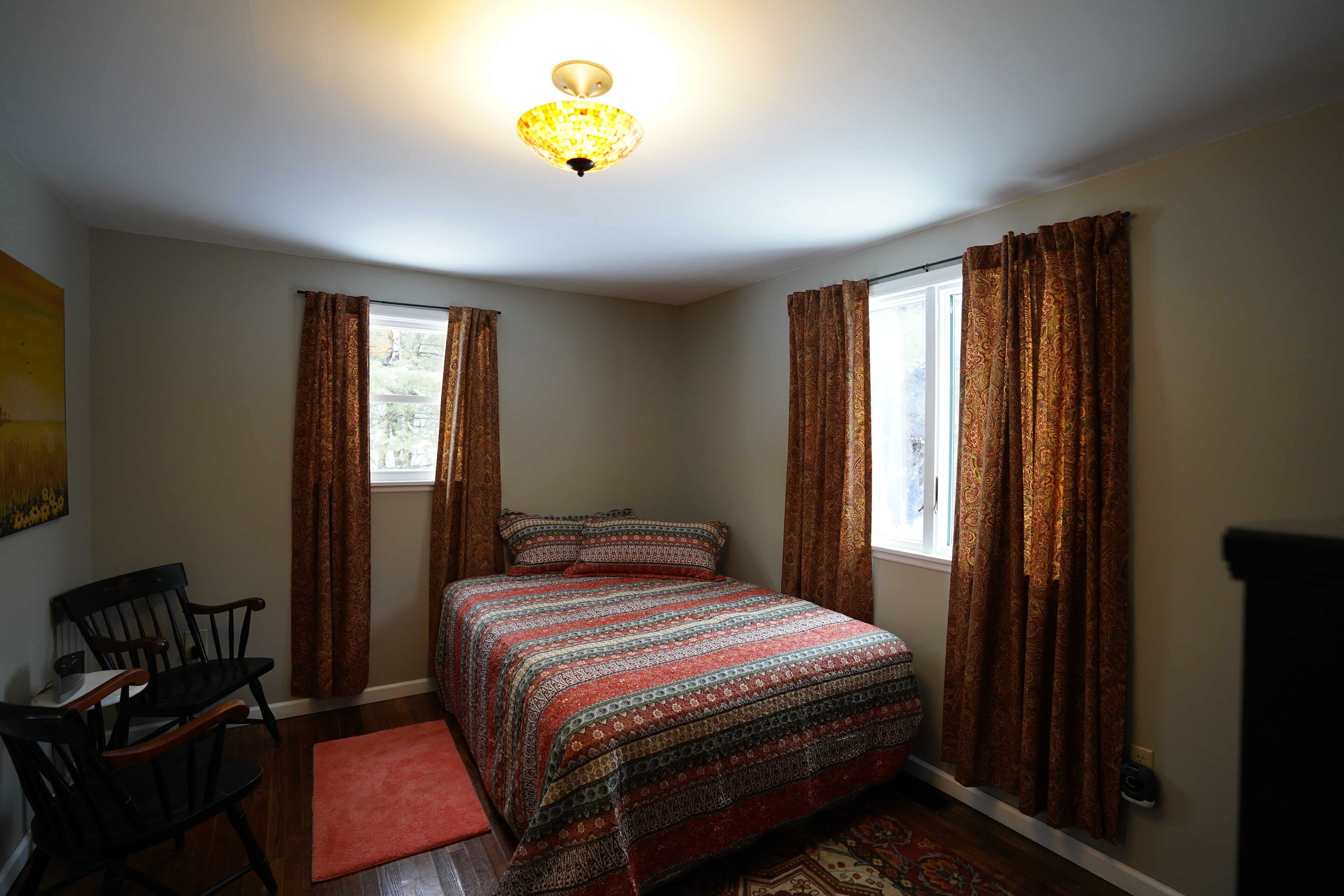 Une chambre à coucher avec un lit, deux chaises, un tapis et une fenêtre avec des rideaux.