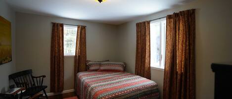 Une chambre à coucher avec un lit, deux chaises, un tapis et une fenêtre avec des rideaux.