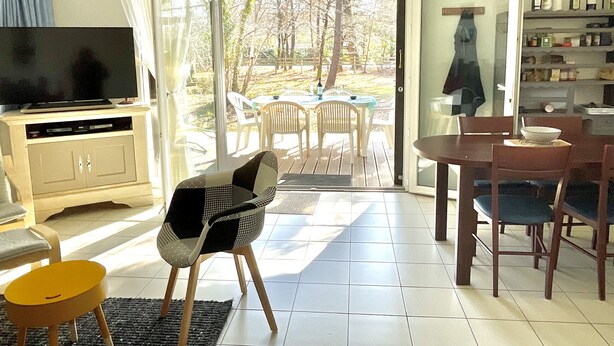 Una sala de estar con televisor, un sofá, una mesa de comedor con sillas y vistas al exterior a través de un ventanal.