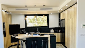 Een moderne keuken met een centraal eiland, zwarte barkrukken, houten kastjes en hanglampen.