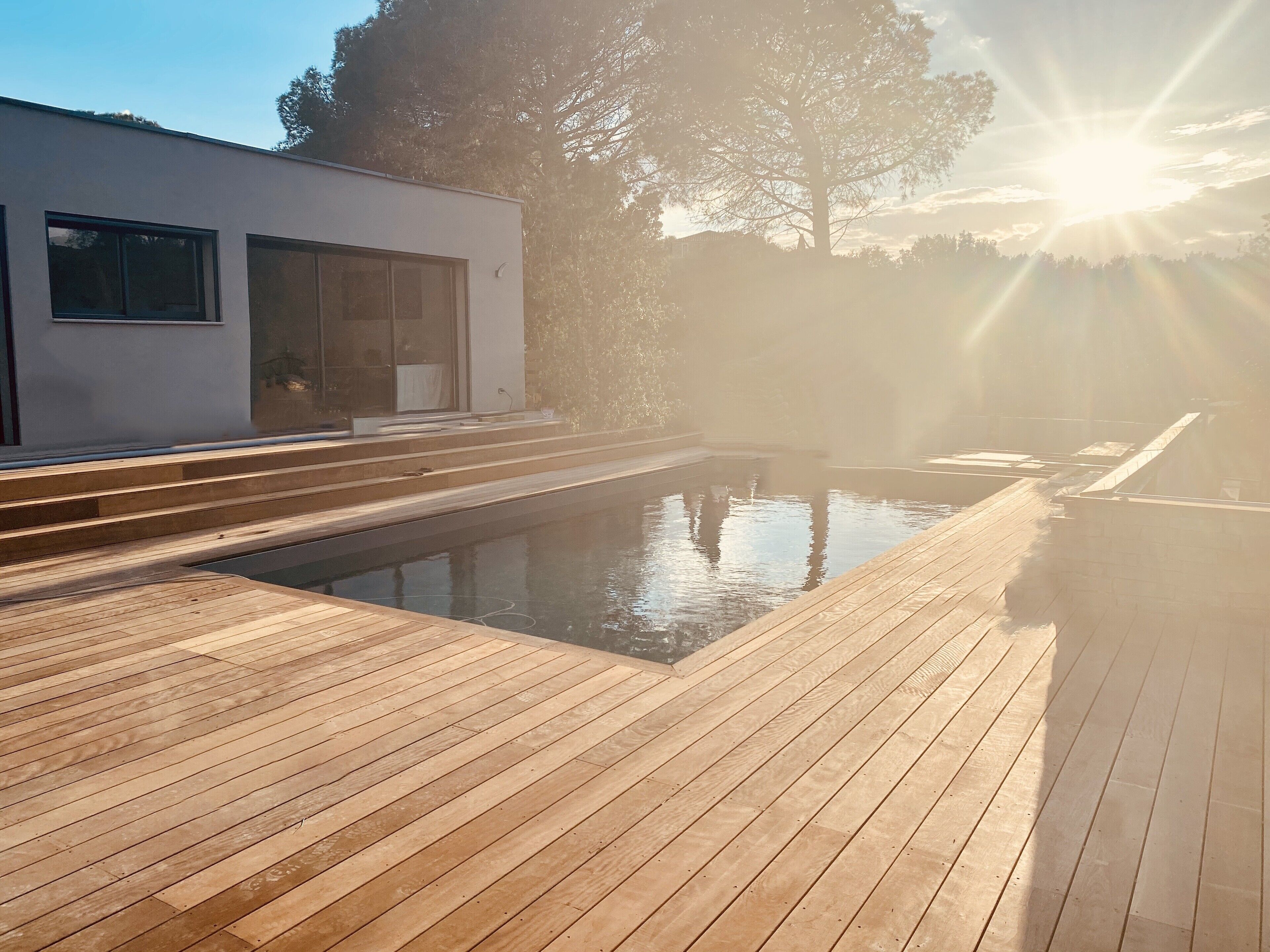 A modern outdoor pool area with wooden decking and a clear view of the surrounding landscape.