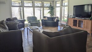 A spacious living room with large windows, a flat-screen TV, and comfortable seating.