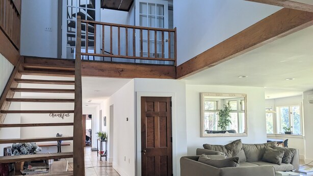 A spacious living area with a wooden staircase, a sofa, and a dining area.