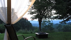 A chair under a sheer canopy with a view of a tree and distant mountains.