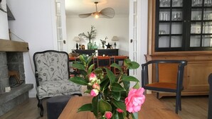 A dining area with a wooden table, a vase with pink flowers, a patterned armchair, and a dining table set with chairs. - Country by the sea! (Tréflaouénan)