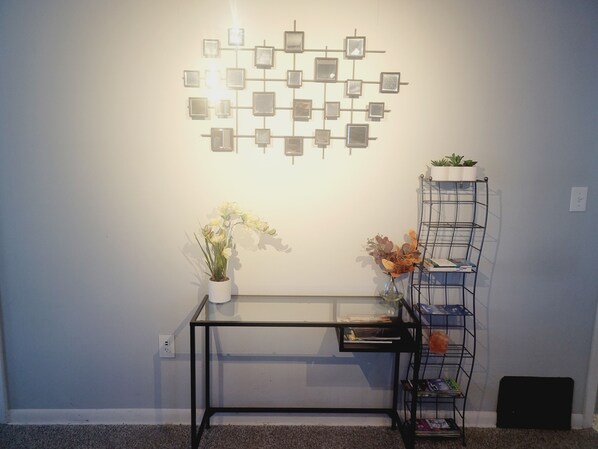 A room with a glass-top table, a metal shelf unit with plants, and a wall-mounted photo display.