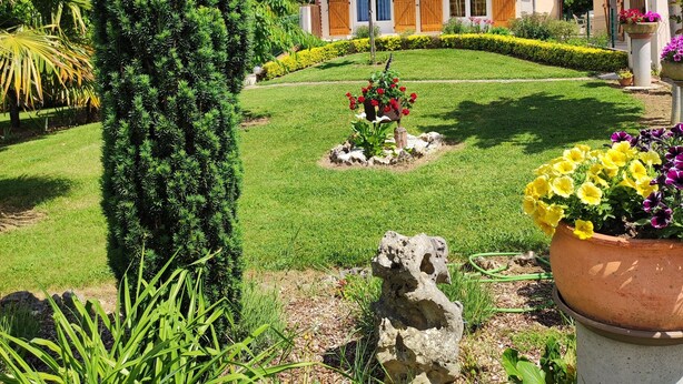 Ein Haus mit Garten, ein hoher Nadelbaum und eine Steinskulptur.