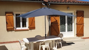Eine Terrasse mit Tisch und Stühlen, ein überdachter Sonnenschirm und ein Haus mit Holzhörnern und einem Ziegeldach.