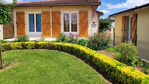 Ein Haus mit Ziegeldach, Holzläden und einem gepflegten Garten mit gelben Blumen und grünen Hecken.