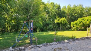 Ein Spielplatz mit Schaukeln und einer Kletterkonstruktion, umgeben von einer Rasenfläche und Bäumen.