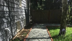Un sendero de grava con borde rojo que lleva a una valla de madera y un árbol.
