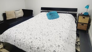Un dormitorio con una cama, una mesita de noche, una lámpara, un cuadro y un sofá.