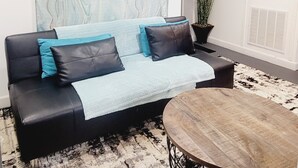 Una sala de estar con un sofá de cuero negro, una manta azul claro y una mesa de centro redonda de madera.