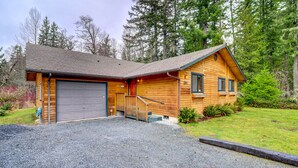 A wooden cabin with a garage, surrounded by trees.