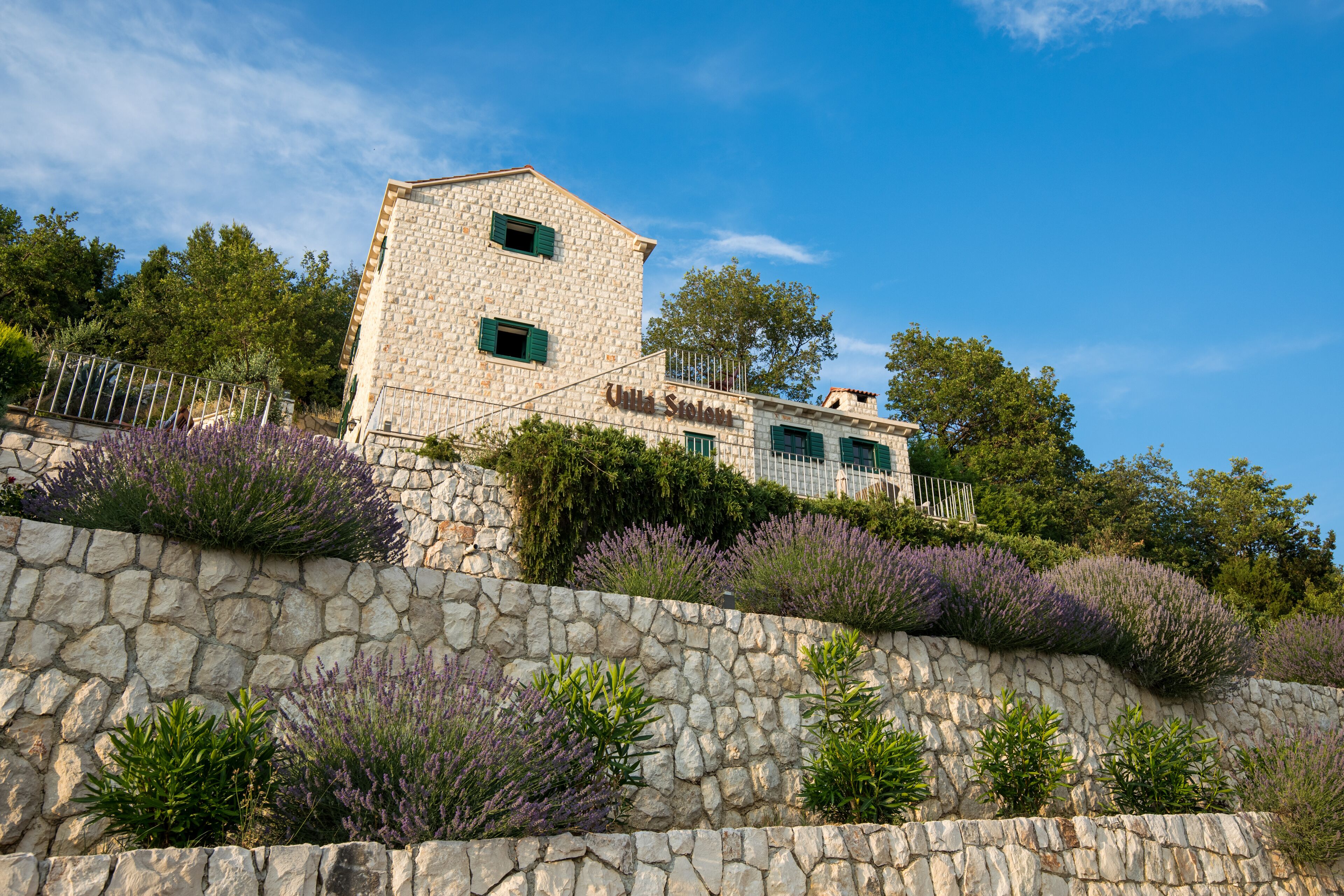 A stone building with a tower, surrounded by lavender plants and trees.