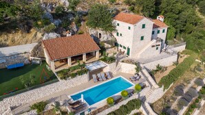 Vista aérea de una villa con piscina, muros de piedra y un jardín en terrazas.