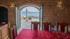 Habitación con paredes de piedra y un arco abierto que da a una terraza con mesa y sillas, un candelabro sobre la mesa y vistas al mar.
