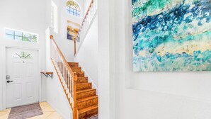 A staircase with wooden steps and white walls, a white door with a window, and a large abstract painting on the wall.
