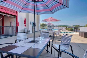Un patio al aire libre con mesas y sillas, sombrillas a rayas y una piscina.