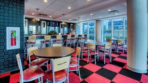 A dining area with round tables and chairs, a fire extinguisher on the wall, and large windows offering a view. - Haven of Rest at Bristol Motor Speedway, Unwind (Bluff City)