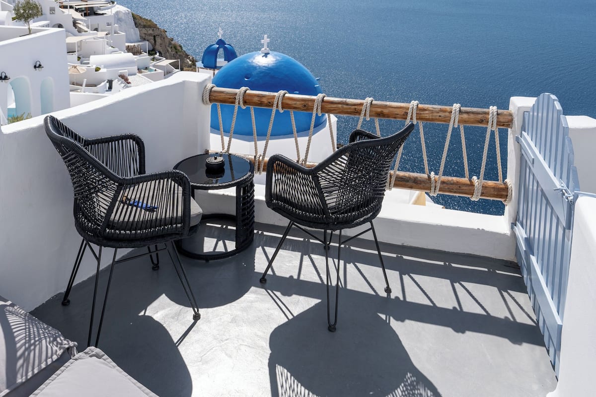 Eine Terrasse mit Tisch und zwei Stühlen mit Blick auf ein Gewässer und eine entfernte Küstenlinie.