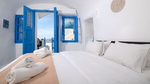 Quarto de hotel com cama, roupa de cama branca, porta azul e vista para o mar.