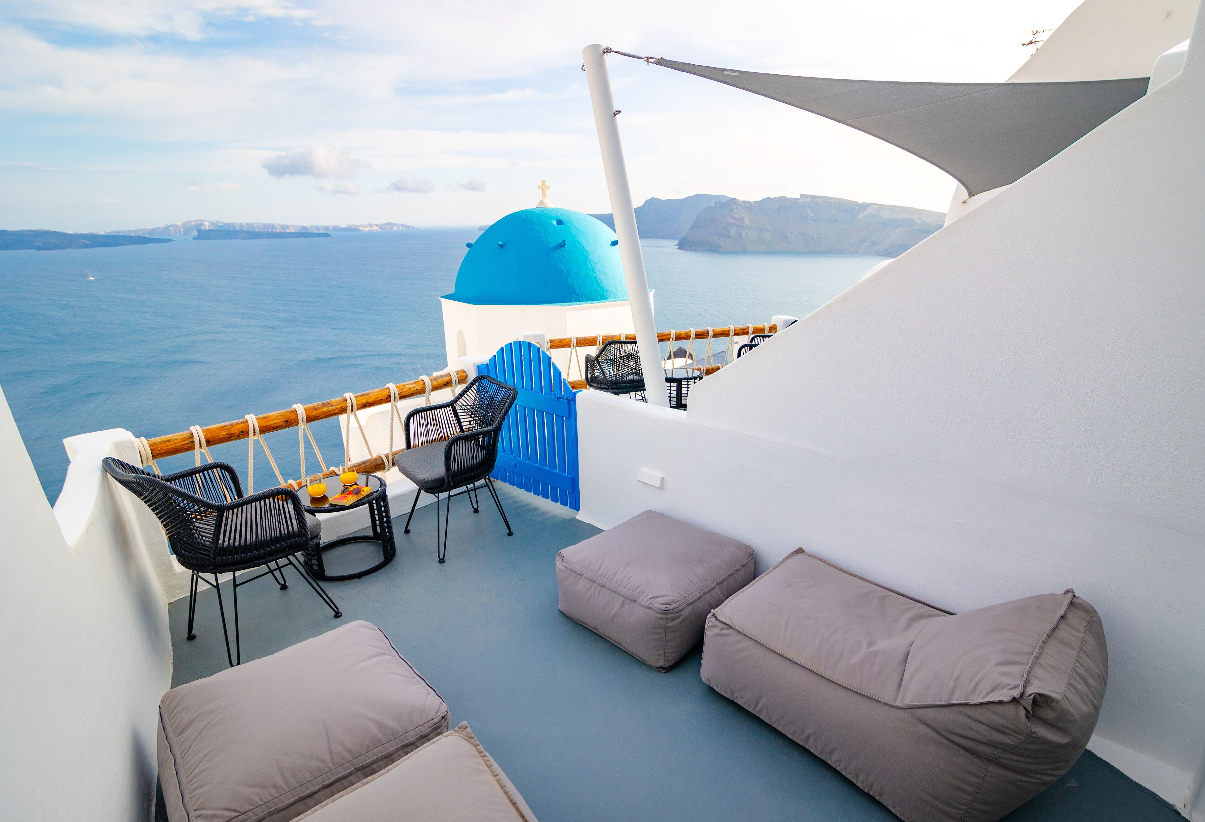 A balcony with a view of the sea, a blue dome, and seating arrangements.