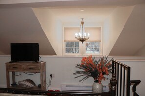 Cozy retreat with a sloped ceiling, chandelier, and comfortable seating area featuring a TV and a vase with fresh flowers.