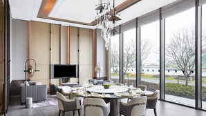 A modern dining area with a round table set for six, a flat-screen TV on the wall, and large windows offering a view of the outdoors. - JW Marriott Shanghai Fengxian (Shanghai)