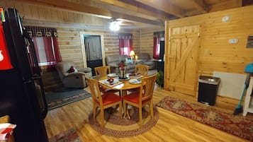 A cozy cabin interior with a wooden dining table, chairs, a sofa, and a fireplace.