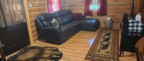 Ein gemütliches Wohnzimmer mit einer schwarzen Ledersofa, Holzboden, einem gemusterten Teppich und einem Klavier.