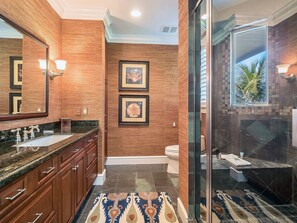 Et moderne badeværelse med et stort spejl, to indrammede billeder, et toilet og en bruseområde med glasvægge.