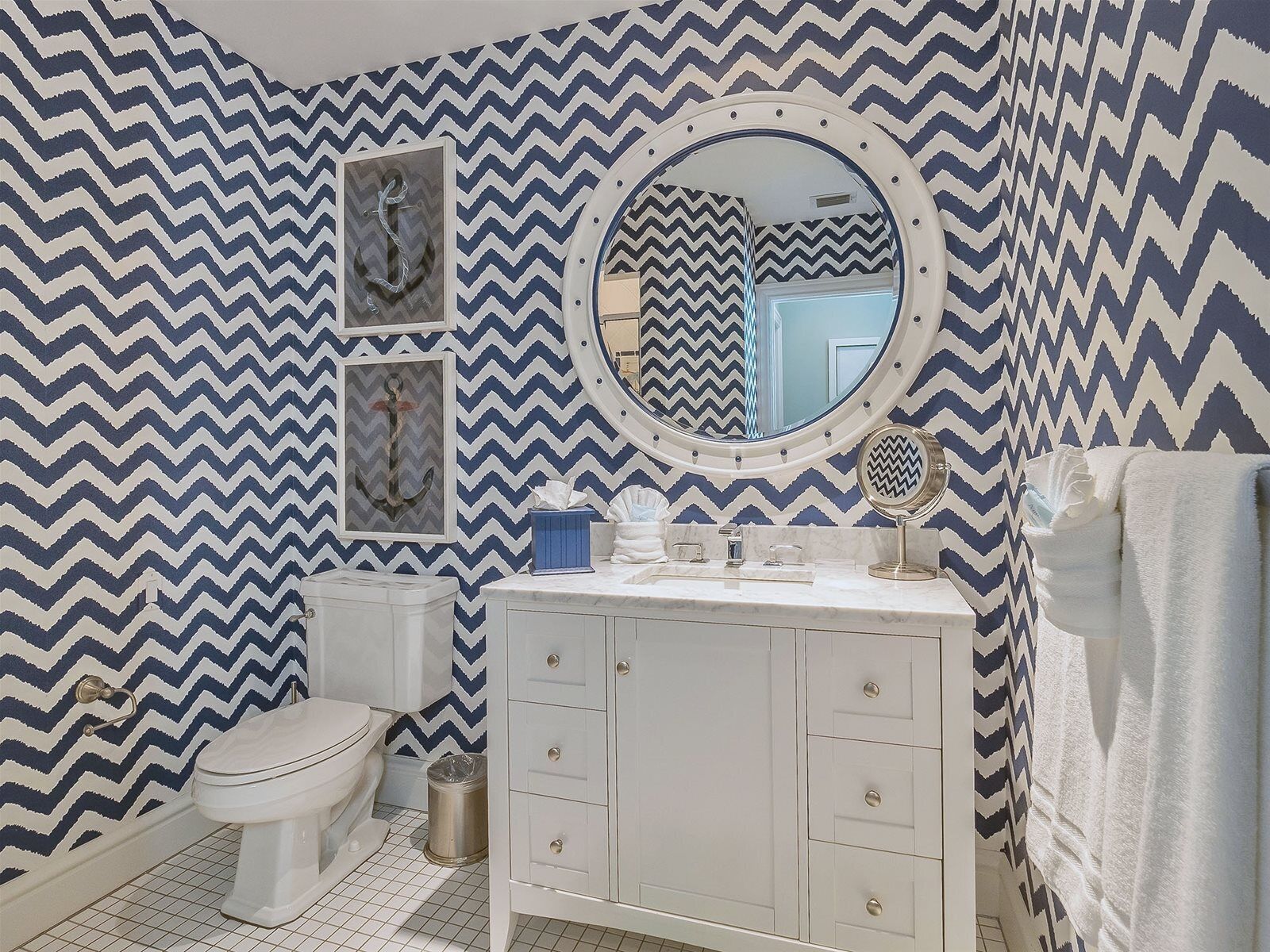 A bathroom with a white vanity, a round mirror, a toilet, and a chevron-patterned wall.