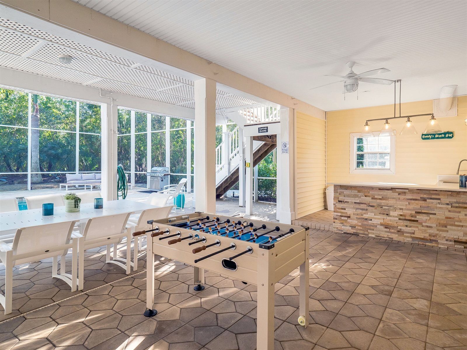 Amplo espaço interno com mesa de futebol, área de estar com mesa e cadeiras, e vista para uma área externa coberta com escada.