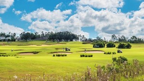 Ein Golfplatz mit Bunkern, blauem Himmel und Bäumen in der Ferne.