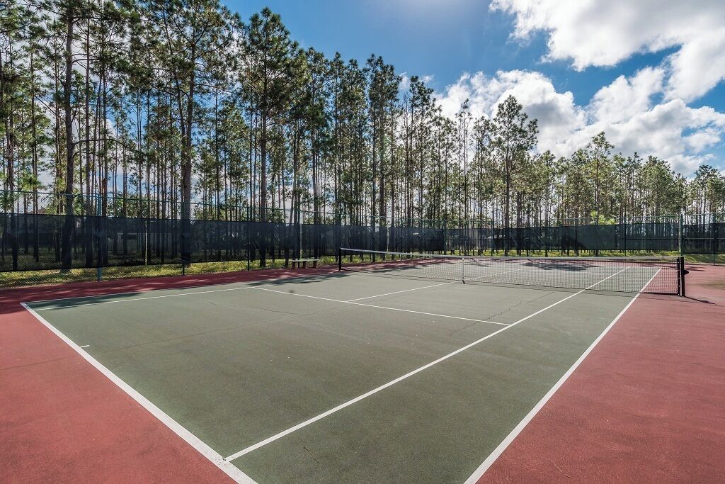 Una cancha de tenis al aire libre con una red, rodeada por una valla y árboles.