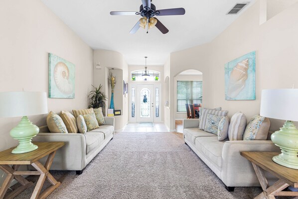 A spacious living room with two sofas, a ceiling fan, and a view of the entrance.