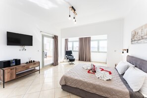 Una habitación de hotel moderna con una cama grande, un televisor de pantalla plana, una mesa consola de madera y un ventanal con cortinas.