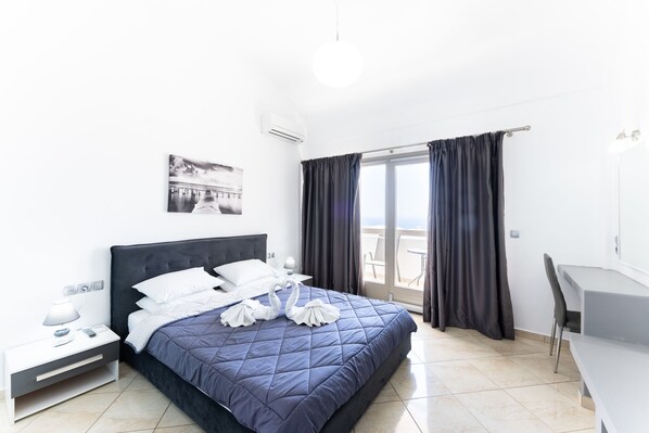 Habitación de hotel moderna con una cama grande, un escritorio y un balcón con cortinas.
