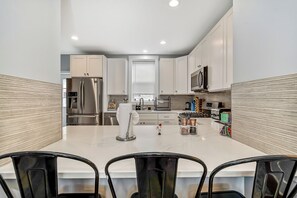 A modern kitchen with white cabinets, stainless steel appliances, and a marble countertop. - Outstanding Home! Relaxing Rooftop+Patio W/Grill (Philadelphia)